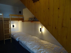 A dormitory room with bunk beds, a ladder, and wall-mounted lights.