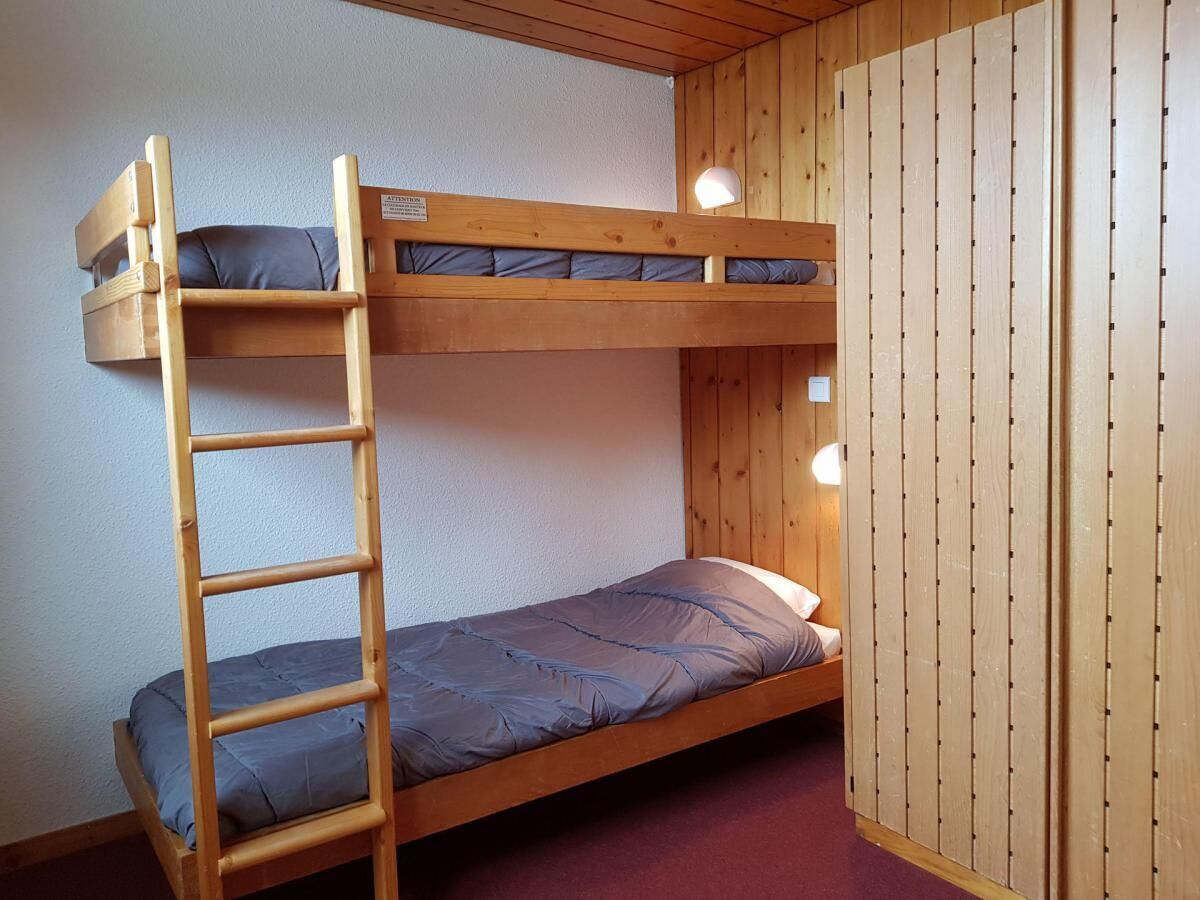 A bunk bed with a ladder, a single bed below, and a wooden wall with a vertical panel design.