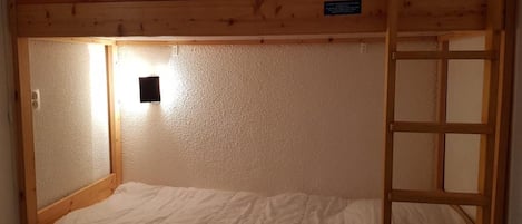 A bunk bed with a wooden frame, a single bed at the bottom, and a ladder on the right side.