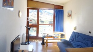 A living room with a blue sofa, a wooden table, and a view of mountains through large windows. - 200m from ski slopes, 11st floor, view mountain, balcony, tv, 28m², Les Arcs (Les Arcs)
