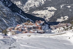 A snow-covered mountain town with multiple buildings, including a hotel with a red roof, situated in a valley surrounded by snow-covered slopes and dense forests.
