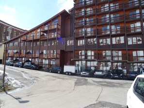 A multi-story hotel with balconies, a parking lot, and several cars parked in front.