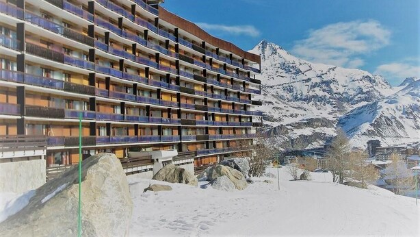 A multi-story hotel with balconies, set against a snowy mountain backdrop.