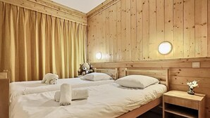 A double bed with white linens, a wooden headboard, and a bedside table with a vase of flowers.
