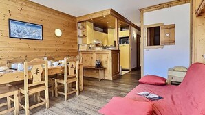 A cozy cabin interior with a dining area, kitchen, and a red sofa.