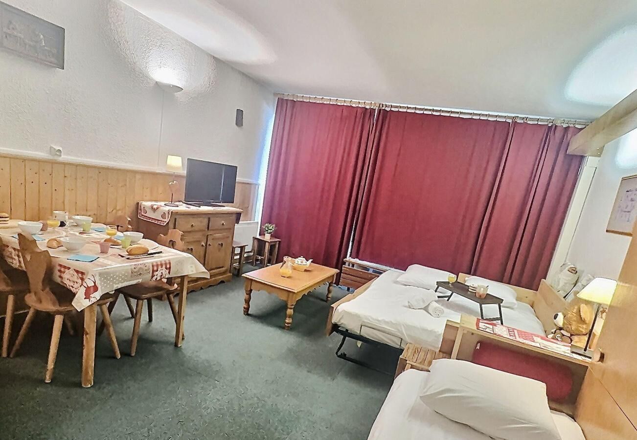 Ett mysigt rum med ett matbord, stolar, en säng, ett litet bord med en lampa och en tv.