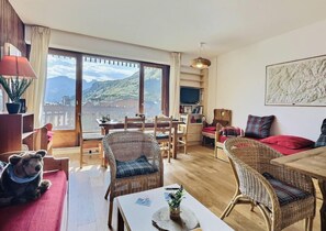 A cozy living room with wicker furniture, a dining area, and a large window offering a view of mountains.