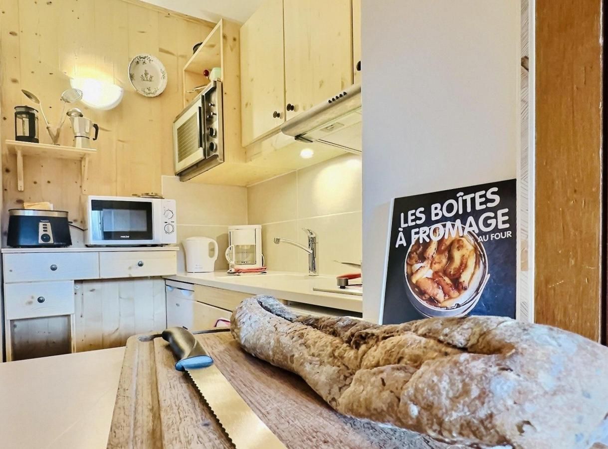 A kitchen with a bread loaf on a wooden board, a microwave, a coffee maker, and a poster on the wall.
