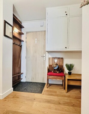 A room with a wooden door, a bench with a teddy bear, a small table with a plant, and a white cabinet.
