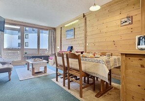 Un coin repas chaleureux avec des murs en bois, une table dressée pour deux personnes et une vue sur l’extérieur grâce à de grandes fenêtres.
