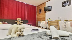 A bedroom with a bed, a teddy bear, a television, and a table with a pitcher and glasses.