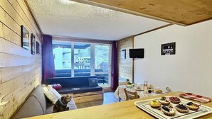 A cozy room with wooden walls, a wooden ceiling, a sofa, a dining table with food, and a view of the outside.