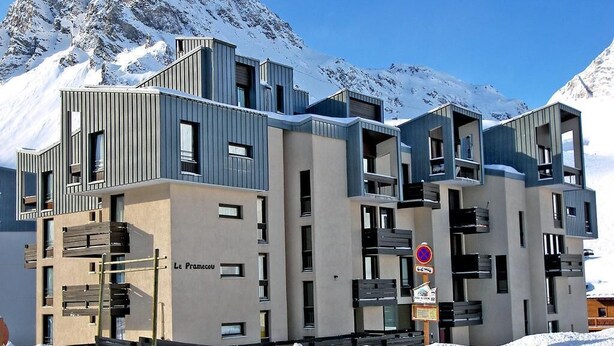 A modern multi-story building with balconies, named "Le Framecou," set against a snowy mountain backdrop.