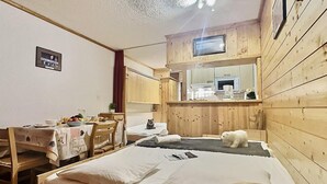 A cozy room with a bed, a desk with a chair, a small table with a bowl of fruit, and a polar bear figurine on the bed.
