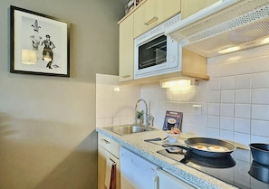 A kitchen with a microwave, sink, and stove. There is a framed picture on the wall and a box of Mini-CocoTttes on the counter.