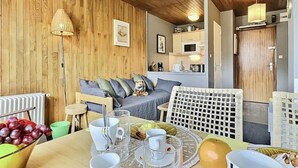 A cozy room with a dining table set for breakfast, a sofa with cushions, and a kitchen area in the background.