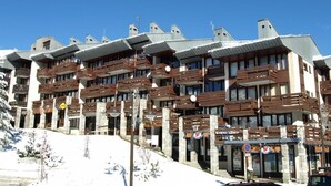 A multi-story hotel with balconies and a ski slope in the background.