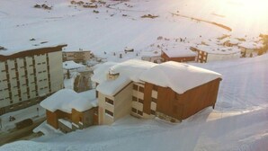 A snow-covered building complex with multiple structures, including a large building with a sloped roof and several smaller buildings with flat roofs. - Ski-in/ski-out & foot of the slopes, 2nd floor, view street, balcony, tv, ski locker, 30m², Tignes (Tignes)