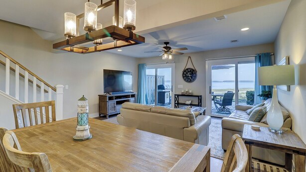 Un vaste espace de vie comprenant une table à manger en bois, des canapés beige, un téléviseur et une vue sur l’extérieur grâce à de grandes portes coulissantes.