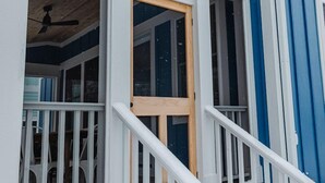 A snow-covered wooden staircase leading to a white door with a glass panel, set against a blue exterior wall.