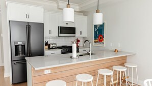 A modern kitchen with white cabinets, stainless steel appliances, a central island with stools, and pendant lighting.