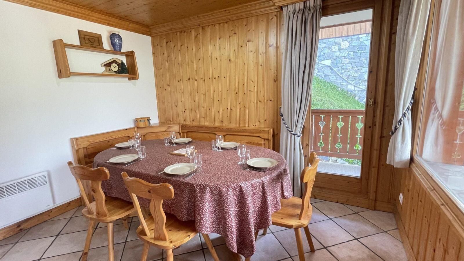Une salle à manger aux murs lambrés, avec une table ronde dressée pour quatre personnes, des chaises et une fenêtre ornée de rideaux.