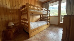 Quarto com beliche de madeira e vista para uma área arborizada.