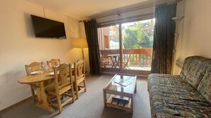 A living room with a wooden dining table, chairs, a sofa, a coffee table, and a TV mounted on the wall. - 250m from ski slopes, 5th floor, view ski slopes, swimming pool, balcony, tv, ski locker, 32m² (Méribel - Les Allues)