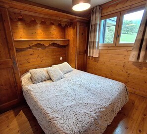 A wooden room with a bed, a window with curtains, and a ceiling light. - 50m from shops, 3rd floor, view mountain, balcony, tv, 43m², Méribel (Méribel - Les Allues)