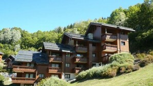 A multi-story wooden building with balconies, set in a hilly, forested area. - 100m from ski slopes, 3rd floor, view mountain, balcony, tv, 43m², Méribel (Méribel - Les Allues)
