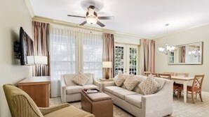 Ein Wohnzimmer mit einer Couch, Sesseln, einem Couchtisch, einem Fernseher und einem Essbereich mit Tisch und Stühlen.