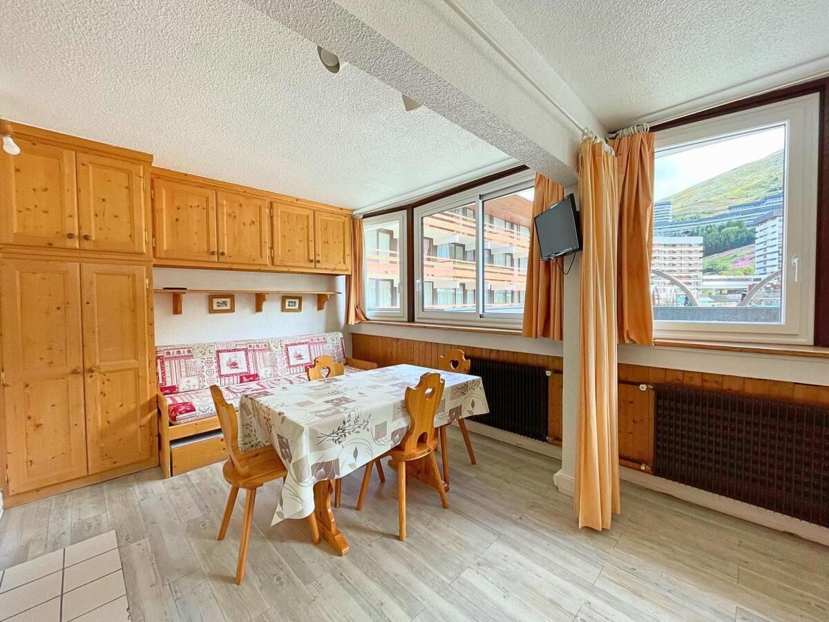 A dining area with a table set for four, wooden cabinets, a radiator, and a window with curtains.
