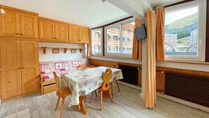 A dining area with a table set for four, wooden cabinets, a radiator, and a window with curtains. - 10m from ski slopes, 1st floor, view resort, tv, ski locker, 24m², Les Menuires (Les Menuires)
