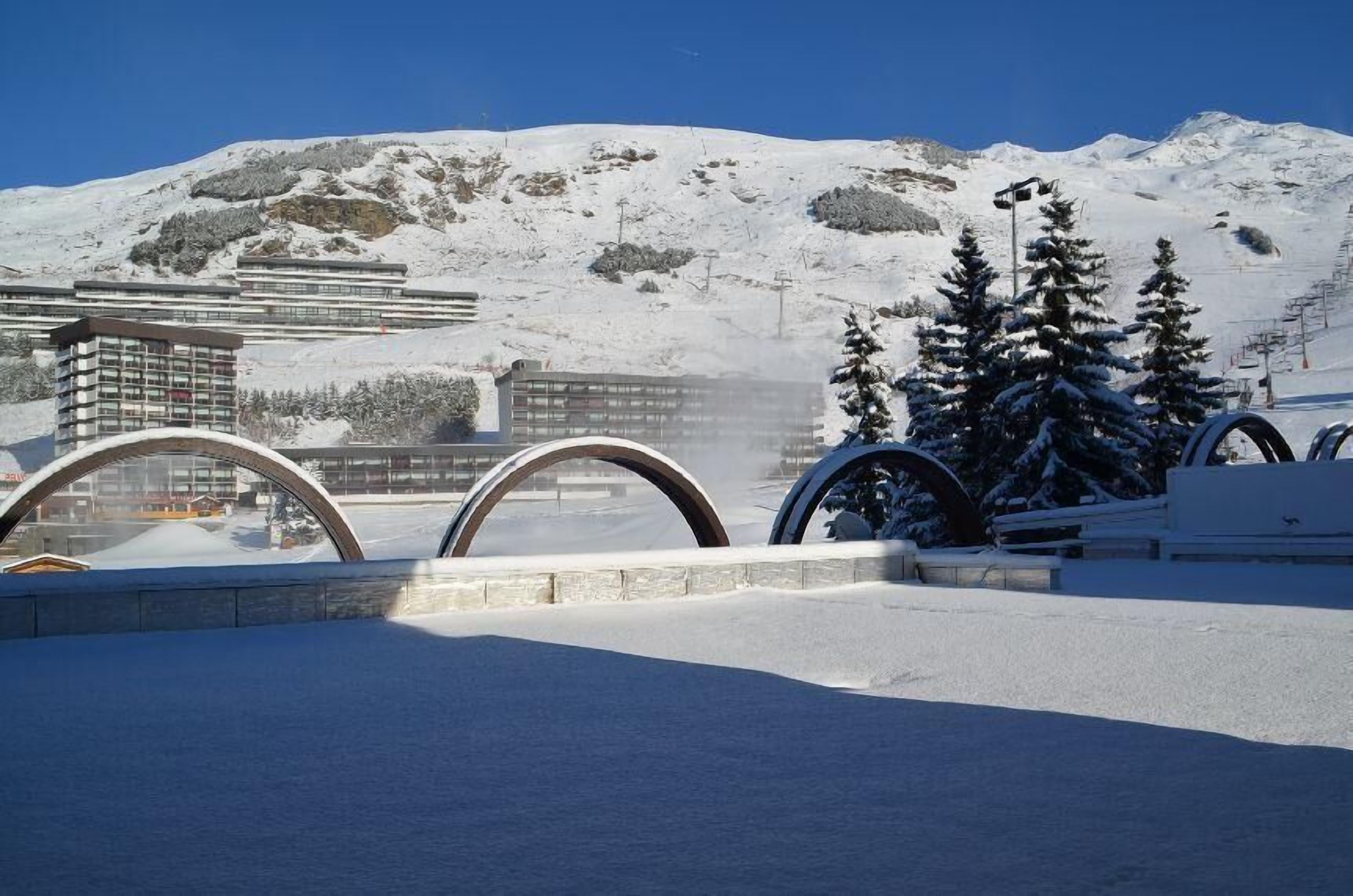 A snow-covered landscape with a ski lift and buildings in the background.