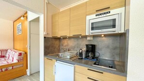 A compact kitchen with wooden cabinets, a built-in microwave, a coffee maker, and a small refrigerator. - 10m from ski slopes, 1st floor, view resort, tv, ski locker, 24m², Les Menuires (Les Menuires)