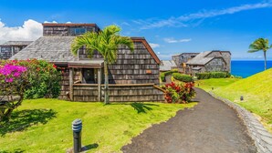 Un bâtiment situé sur la côte, doté d’un toit en pente, entouré d’une végétation luxuriante et offrant une vue dégagée sur l’océan.