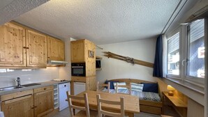 Une pièce de taille modeste, dotée de meubles en bois, d’un coin cuisine, d’une table à manger avec des chaises, d’un lit avec une tête de lit et d’une fenêtre avec des rideaux.