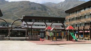 Un hôtel situé au pied d’une montagne, doté d’un terrain de jeux avec des équipements colorés et d’un toboggan vert.