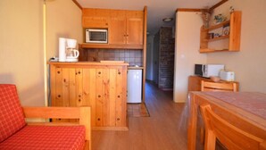 Eine kleine Küche mit Holzausstattung, einer Mikrowelle, einer Kaffeemaschine und einem Kühlschrank.