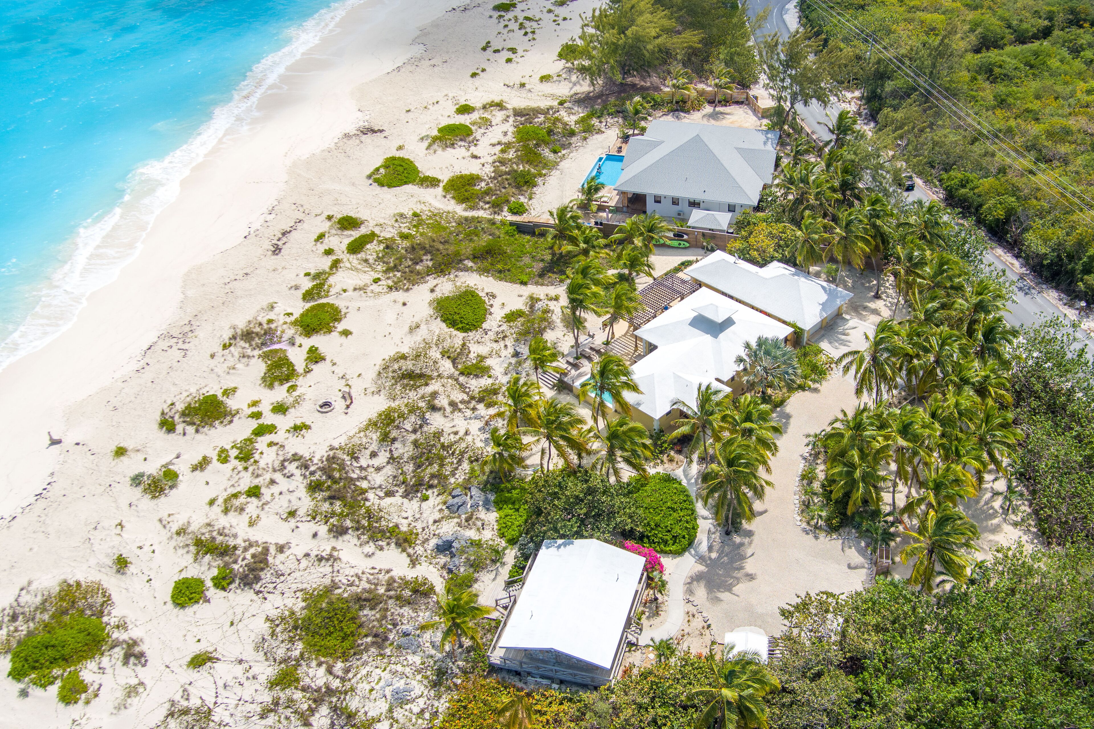 Vue aérienne d’une propriété située en bord de mer, avec une grande maison, une piscine et plusieurs palmiers.
