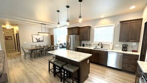 A modern kitchen with a central island, bar stools, a dining area, and a view into the living room. - Serenity Now @ Spring Brook Resort (Wisconsin Dells)
