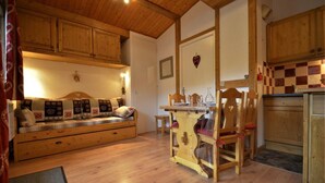 Una camera accogliente con soffitto in legno, un divano con cuscini decorati, un tavolo da pranzo con sedie e un angolo cottura con mobili in legno.