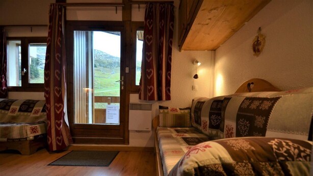 Una stanza accogliente con pavimento in legno, un divano con cuscini decorati, una finestra con tende e un punto luce a parete.