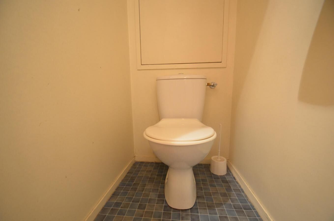 Een kleine, schone badkamer met toilet, toiletborstel en betegelde vloer.