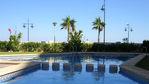 A swimming pool with clear blue water, surrounded by palm trees and a well-maintained garden. - Apartamento Da Vinci 5 Inmomart (Peñiscola)