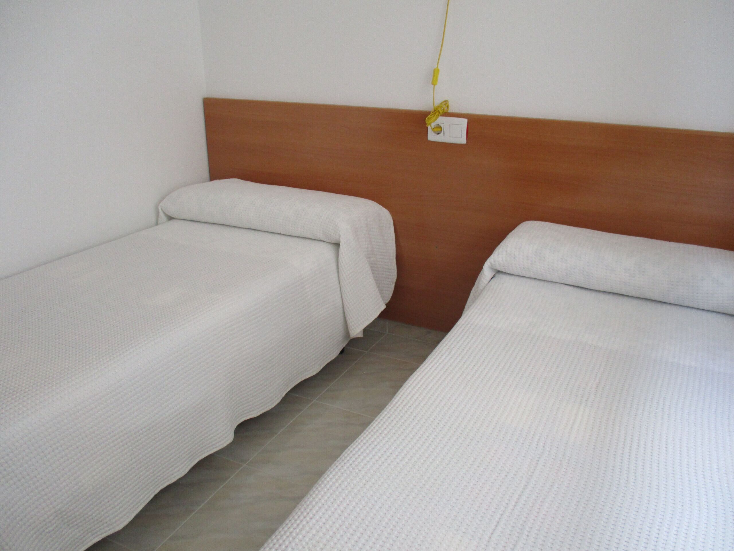 Two single beds with wooden headboards in a room with tiled flooring.