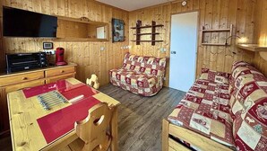 L’intérieur chaleureux d’un chalet avec des murs en bois, une table à manger avec des chaises, un canapé et un téléviseur.