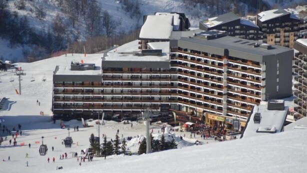 Un hôtel à plusieurs étages doté de balcons, offrant un accès direct aux pistes de ski et surplombant un paysage montagneux enneigé.