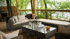 A covered outdoor seating area with wicker furniture, a glass coffee table, and a view of the trees. - 12 Loch View PF Kenmore (Aberfeldy)