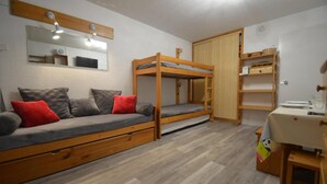 A compact room with a bunk bed, a sofa with storage drawers, a small table, and a mirror. - 10m from ski slopes, 8th floor, balcony, tv, 24m², Les Menuires (Les Menuires)